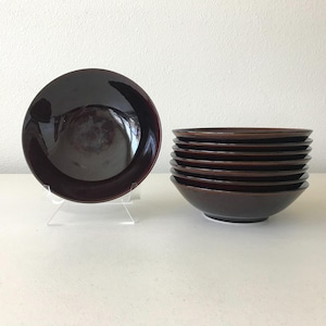 May include: A set of dark brown ceramic bowls. One bowl is displayed on a clear stand, while the others are stacked. The bowls have a glossy finish and a simple, modern design, suitable for serving various dishes.