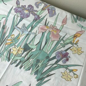 May include: White fabric with a floral pattern featuring irises in shades of purple, pink, and yellow, along with green leaves and stems. The design includes dragonflies. A soft, botanical theme.