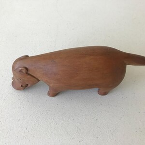 K&ouml;nnte beinhalten: Holzskulptur eines Capybaras mit polierter Oberfl&auml;che. Die braune Figur hat einen abgerundeten K&ouml;rper, kurze Beine und einen kleinen Schwanz. Das Capybara ist in einer entspannten Pose dargestellt, mit leicht gesenktem Kopf.