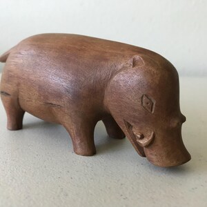 K&ouml;nnte beinhalten: Eine handgeschnitzte Holzfigur eines Nilpferds. Das braune Nilpferd hat ein detailliertes Design mit sichtbaren geschnitzten Merkmalen. Die Figur steht auf vier Beinen, mit gesenktem Kopf. Die Holzmaserung ist sichtbar.