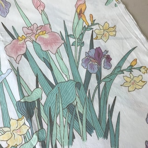May include: White fabric with a floral pattern featuring irises in shades of pink, purple, and yellow, with green leaves and stems. The design has a vintage, hand-drawn aesthetic, suitable for fabric or home decor.