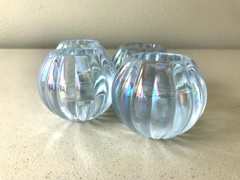 May include: A set of three small, spherical glass candle holders featuring a vertical ribbed texture and an iridescent finish that reflects light with subtle blue and purple hues. Each piece has a wide circular opening at the top.