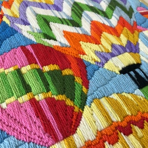 May include: Close-up of a colorful, embroidered artwork featuring hot air balloons. The balloons are in various colors, including pink, green, orange, and yellow, with a blue sky background. The piece is framed.
