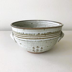 May include: A set of three ceramic mugs with a speckled, matte finish. The mugs are in shades of cream, light gray, and dark gray. Each mug has a simple, minimalist design and a rounded handle.