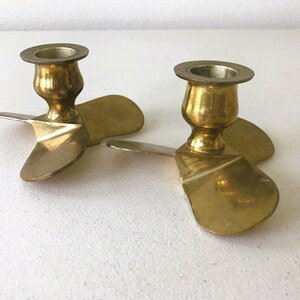 Puede incluir: Dos candelabros de metal dorado con forma de h&eacute;lice. Cada candelabro tiene tres aspas y una base redonda.