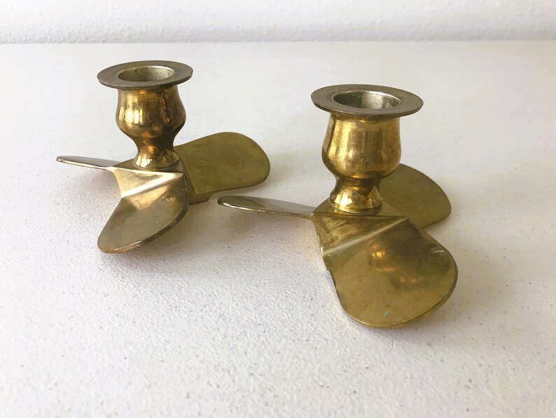 Puede incluir: Dos candelabros de metal dorado con forma de h&eacute;lice. Cada candelabro tiene tres aspas y una base redonda.