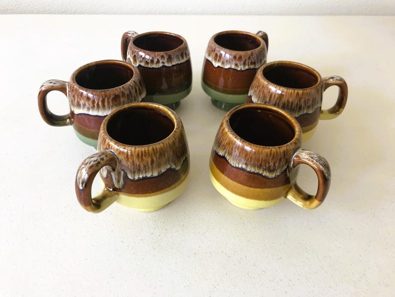 May include: Six brown and yellow ceramic mugs with a glazed finish. The mugs have a rounded shape and a handle on the side.
