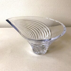 Pode incluir: Uma tigela decorativa de vidro transparente com uma forma assim&eacute;trica &uacute;nica. A tigela apresenta uma base alargada que se estreita para cima, com uma borda curva. O interior tem uma s&eacute;rie de linhas curvas gravadas. A tigela &eacute; feita de vidro transparente.