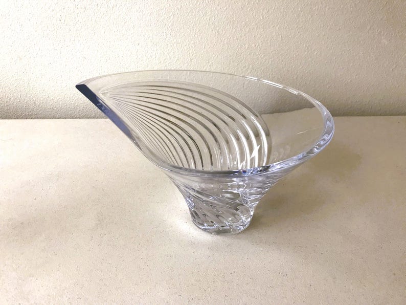 Pode incluir: Uma tigela decorativa de vidro transparente com uma forma assim&eacute;trica &uacute;nica. A tigela apresenta uma base alargada que se estreita para cima, com uma borda curva. O interior tem uma s&eacute;rie de linhas curvas gravadas. A tigela &eacute; feita de vidro transparente.