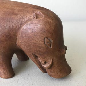K&ouml;nnte beinhalten: Handgeschnitzte Holzfigur eines Flusspferds in Braun. Die Skulptur weist detaillierte Schnitzereien auf, darunter Augen, Ohren und Maul des Flusspferds. Die Figur ist ein dekoratives Objekt, das die nat&uuml;rliche Holzmaserung zeigt.