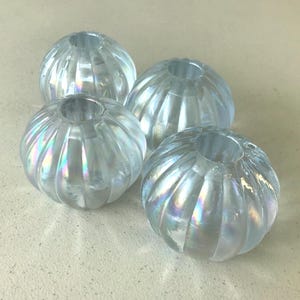 May include: Four round, translucent glass beads with a ribbed, pumpkin-like texture. Each bead features an iridescent, pearlescent finish that reflects light with subtle rainbow hues. The beads have a central hole for threading and a clear, glossy surface.