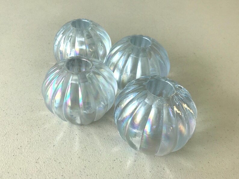 May include: Four round, translucent glass beads with a ribbed, pumpkin-like texture. Each bead features an iridescent, pearlescent finish that reflects light with subtle rainbow hues. The beads have a central hole for threading and a clear, glossy surface.