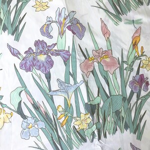 May include: White fabric with a floral pattern featuring irises in shades of purple, pink, and blue, along with yellow flowers and green foliage. The design includes dragonflies. The fabric is likely used for home decor or apparel.