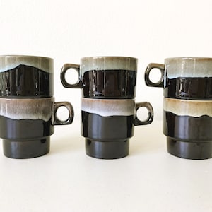 May include: Set of six brown and white ceramic coffee mugs with a layered glaze design. The mugs are stacked in pairs.