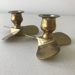 Puede incluir: Un par de candelabros de lat&oacute;n con forma de h&eacute;lices de avi&oacute;n. Los candelabros est&aacute;n conectados en el centro y tienen un dise&ntilde;o cl&aacute;sico.
