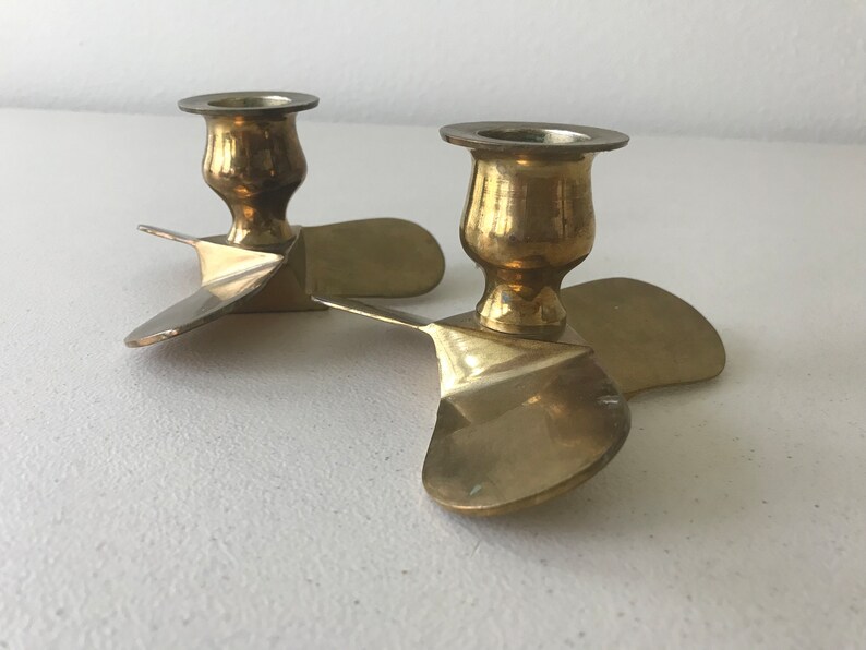 Puede incluir: Un par de candelabros de lat&oacute;n con forma de h&eacute;lices de avi&oacute;n. Los candelabros est&aacute;n conectados en el centro y tienen un dise&ntilde;o cl&aacute;sico.