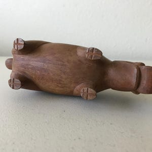 K&ouml;nnte beinhalten: Eine braune Holzskulptur eines Nilpferds, das auf dem R&uuml;cken liegt. Die Skulptur hat vier Beine mit kreuzf&ouml;rmigen Details an den F&uuml;&szlig;en. Der K&ouml;rper des Nilpferds ist glatt und abgerundet, mit einem kleinen Schwanz und einem abgerundeten Kopf.
