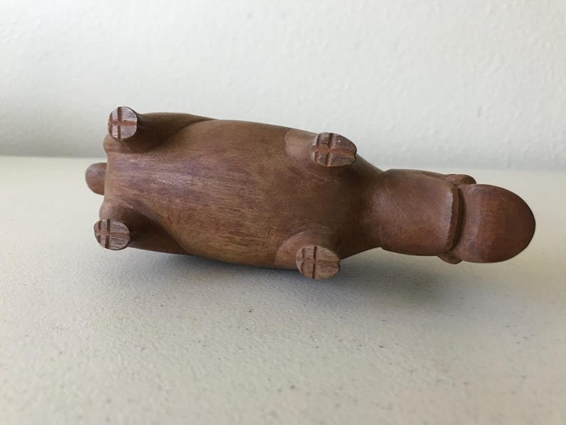 K&ouml;nnte beinhalten: Eine braune Holzskulptur eines Nilpferds, das auf dem R&uuml;cken liegt. Die Skulptur hat vier Beine mit kreuzf&ouml;rmigen Details an den F&uuml;&szlig;en. Der K&ouml;rper des Nilpferds ist glatt und abgerundet, mit einem kleinen Schwanz und einem abgerundeten Kopf.