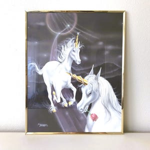 May include: Framed print featuring two white unicorns with golden horns against a dark, starry background. One unicorn is running, and the other holds a red rose in its mouth. The artwork is in a gold-colored frame.