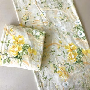May include: A folded sheet and a long, unfolded sheet with a floral pattern. The pattern features large yellow roses, white daisies, and green leaves on a cream-colored background. The sheets have a vintage aesthetic.