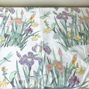 May include: White fabric with a floral pattern featuring purple, pink, and yellow irises, green leaves, and light green dragonflies. The design is repeated across the fabric, creating a garden-like scene.