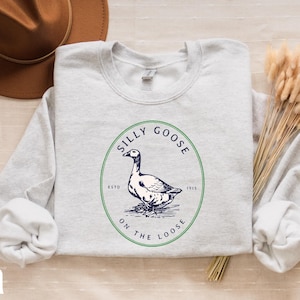 May include: A light gray sweatshirt with a green circle graphic featuring a goose and the text "Silly Goose on the Loose" in navy blue.