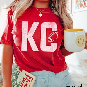 A simple textured looking KC printed on a soft and durable comfort colors 1717 tshirt- with an outline of a football in the letter C- perfect for game day or any Red Friday in Kansas City to celebrate the Chiefs
