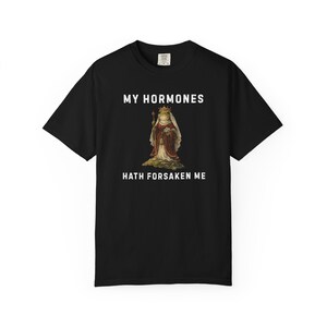 May include: Black t-shirt with the text "MY HORMONES HATH FORSAKEN ME" in white. The shirt features a graphic of a frog wearing a crown and royal attire, holding a staff. The t-shirt is a crew neck style.