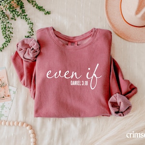 May include: A crimson long-sleeve crewneck sweatshirt featuring the white text "even if" in a cursive script font, followed by the text "DANIEL 3:18" in a clean sans-serif font. The sweatshirt has a ribbed collar and cuffed sleeves.