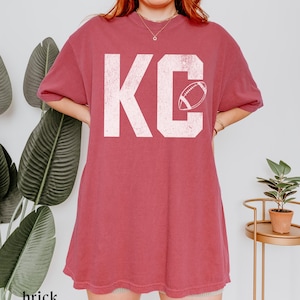 A simple textured looking KC printed on a soft and durable comfort colors 1717 tshirt- with an outline of a football in the letter C- perfect for game day or any Red Friday in Kansas City to celebrate the Chiefs