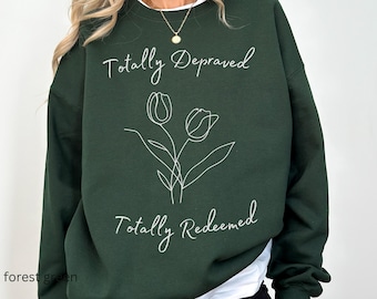 May include: A dark green sweatshirt with the text "Totally Depraved" and "Totally Redeemed" in white. The sweatshirt features a simple line drawing of two tulips.