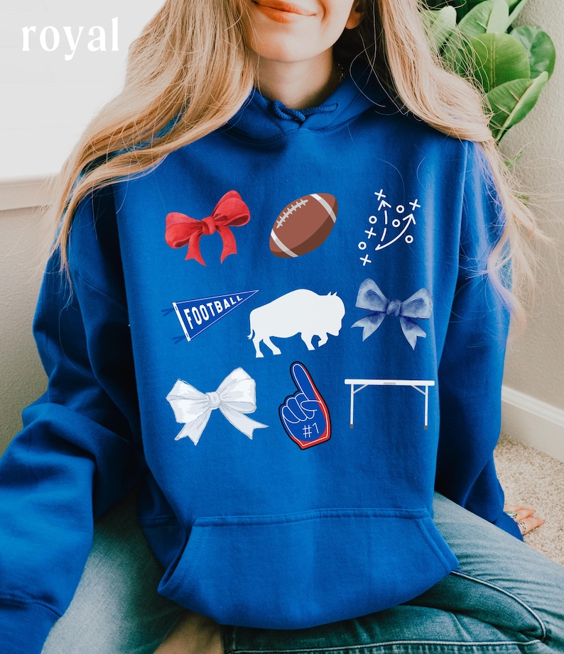 Puede incluir: Una sudadera con capucha azul real con una variedad de aplicaciones blancas, rojas y azules. Las aplicaciones incluyen un bal&oacute;n de f&uacute;tbol, un b&uacute;falo, un lazo, un bander&iacute;n, una mesa y un dedo &iacute;ndice con el n&uacute;mero uno.