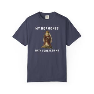 May include: Navy blue t-shirt featuring the text "MY HORMONES HATH FORSAKEN ME" with a vintage illustration of a frog in regal clothing. A comfortable, casual wear item.