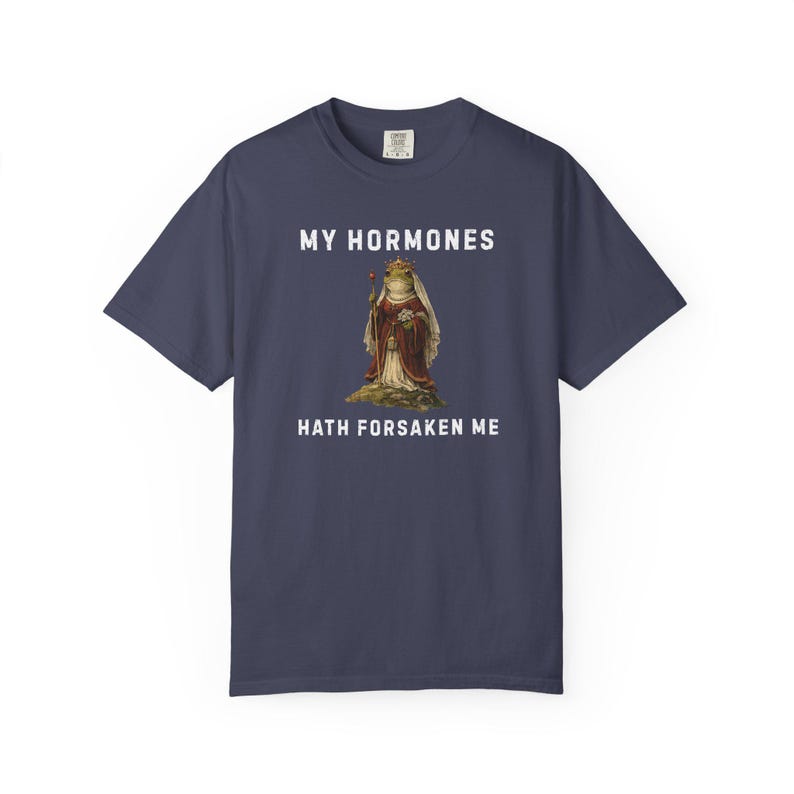 May include: Navy blue t-shirt featuring the text "MY HORMONES HATH FORSAKEN ME" with a vintage illustration of a frog in regal clothing. A comfortable, casual wear item.