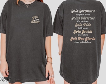 May include: Dark gray t-shirt with "The Five Solas" printed on the front and a list of the five solas on the back. The text is in a light brown color. The shirt is a casual, oversized fit.