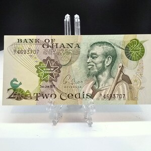 May include: A two Cedi banknote from Ghana, featuring a portrait of a man with a beard and a traditional Ghanaian outfit. The note is dated 2nd Jan 1977 and has the text "Bank of Ghana" and "Two Cedis" printed on it.