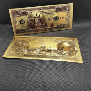 Puede incluir: Dos billetes dorados de fantasía, cada uno con el texto "ONE MILLION" y "THE UNITED STATES OF AMERICA". Los billetes tienen diseños detallados, incluyendo una representación de la Estatua de la Libertad y el Capitolio de los Estados Unidos.
