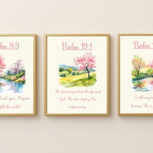 Puede incluir: Tres impresiones enmarcadas en acuarela con paisajes con árboles florecientes rosas y naranjas, un río y textos de Salmos. Los marcos son dorados. El texto incluye Salmo 8:9, Salmo 19:1 y Salmo 13:6.
