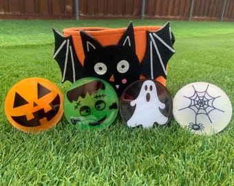 May include: Four Halloween-themed, round, flat, plastic decorations. The decorations feature a jack-o'-lantern, a Frankenstein monster, a ghost, and a spider web with a spider.