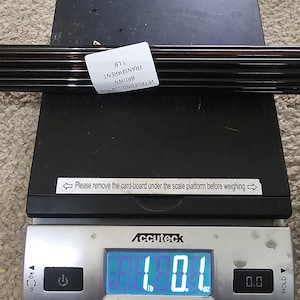 Puede incluir: Una báscula digital muestra 0,45 kg. Varias varillas de vidrio marrón transparente están apiladas en la báscula. Una etiqueta dice "BROWN TRANSPARENT 1 LB VETROFOND 104 COE". La báscula es negra y tiene una pantalla digital.