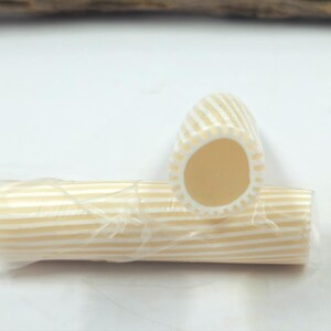 May include: Two cylindrical beads featuring a cream and white striped pattern. One bead is positioned horizontally, while the other is placed vertically, showing its hollow center. Both beads are wrapped in a thin, clear plastic film.