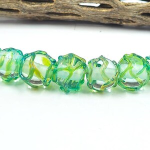 May include: A strand of seven spherical glass beads, each featuring a clear base with an intricate, raised lattice pattern in shades of vibrant green and teal, with subtle yellow accents visible within the core of the transparent glass spheres.