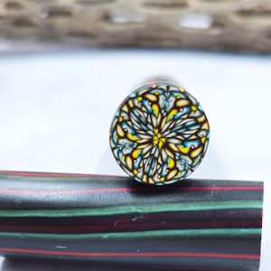 Puede incluir: Primer plano de un bolígrafo decorativo. El extremo del bolígrafo presenta un intrincado diseño floral en amarillo, azul y blanco. El cuerpo del bolígrafo está rayado con rojo, verde y negro.
