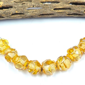 May include: A strand of eight translucent amber-colored glass beads, each featuring a distinct swirling pattern of opaque white glass lines. The beads are arranged in a gentle arc, showcasing a glossy finish and a rounded, multifaceted shape.