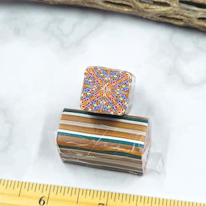 Puede incluir: Dos bloques de arcilla polimérica. Uno es un cubo con un diseño floral colorido. El otro es un bloque rectangular con rayas horizontales en tonos marrón, beige y verde azulado. Ambos están envueltos en plástico transparente.