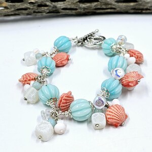May include: A turquoise and coral beaded bracelet with a silver clasp. The bracelet features various sized beads, including shell-shaped charms and square beads.
