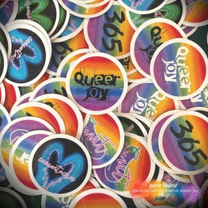 Könnte beinhalten: Eine Ansammlung runder Aufkleber mit Regenbogen-Verlaufs-Hintergründen. Einige Aufkleber zeigen den Text "Queer Joy" in Schwarz, während andere "365" oder andere Designs zeigen. Die Aufkleber haben einen weißen Rand und verschiedene Designs.