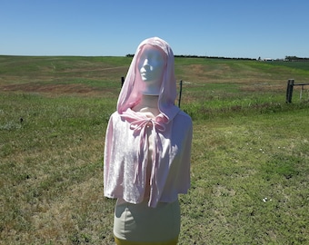 May include: A pink hooded cape with a tie at the neck. The cape is made of a soft, velvety fabric.