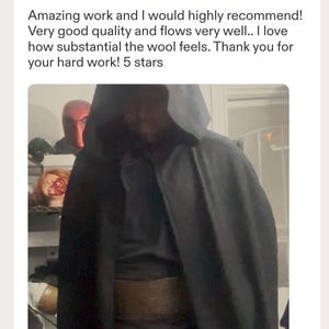 May include: A dark charcoal gray hooded cloak made of a substantial wool fabric. The garment features a deep hood and a wide, textured brown belt worn around the waist. The cloak drapes over the shoulders and hangs down to cover the torso area.