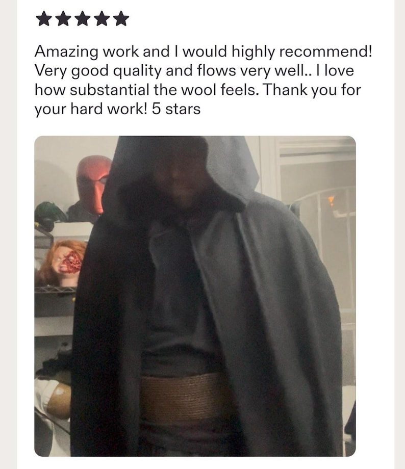 May include: A dark charcoal gray hooded cloak made of a substantial wool fabric. The garment features a deep hood and a wide, textured brown belt worn around the waist. The cloak drapes over the shoulders and hangs down to cover the torso area.